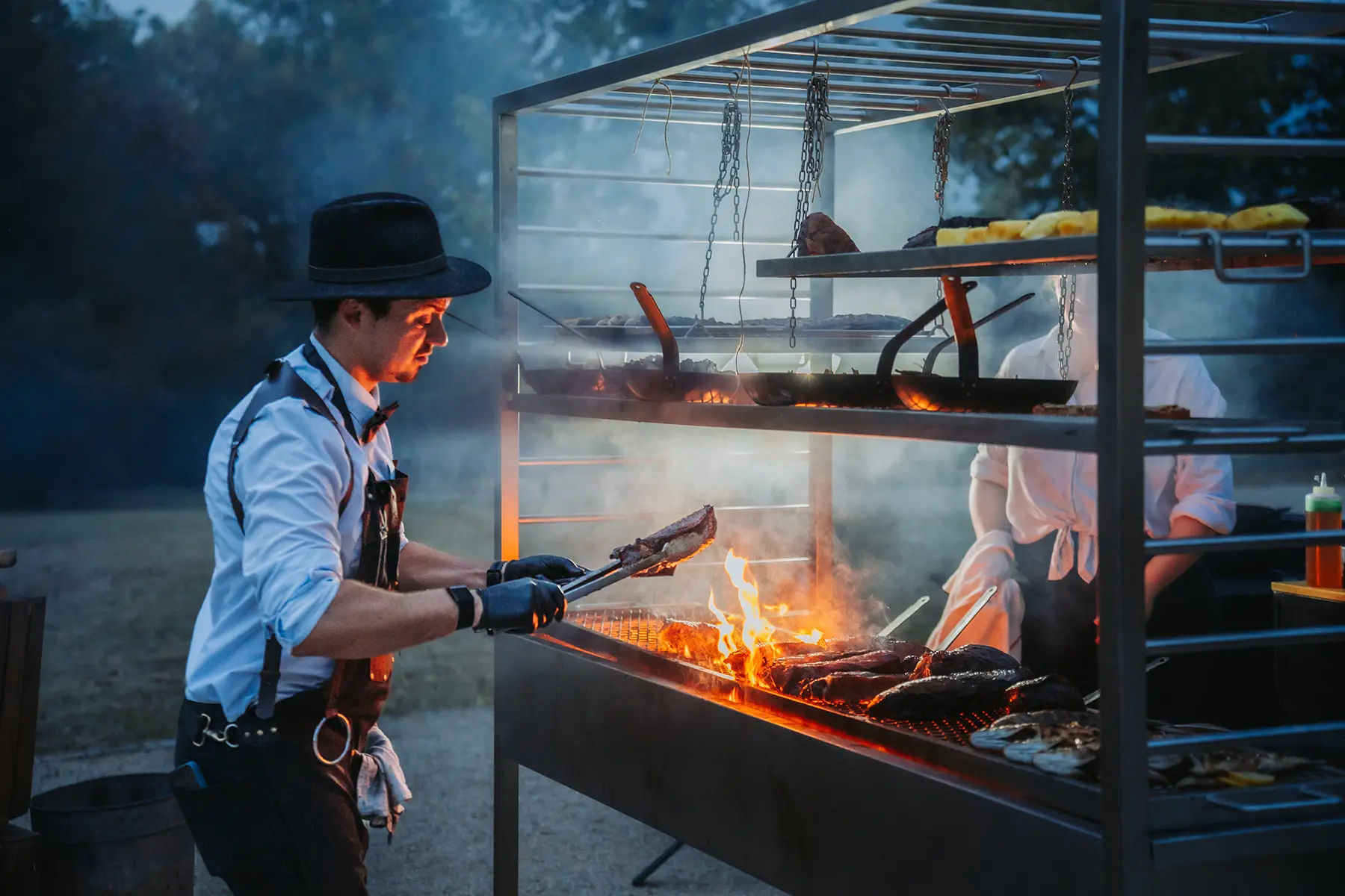 Aurélie & Jérémy 101 Cuisinier en chapeau et tablier manipulant de la viande sur un grand barbecue à étages