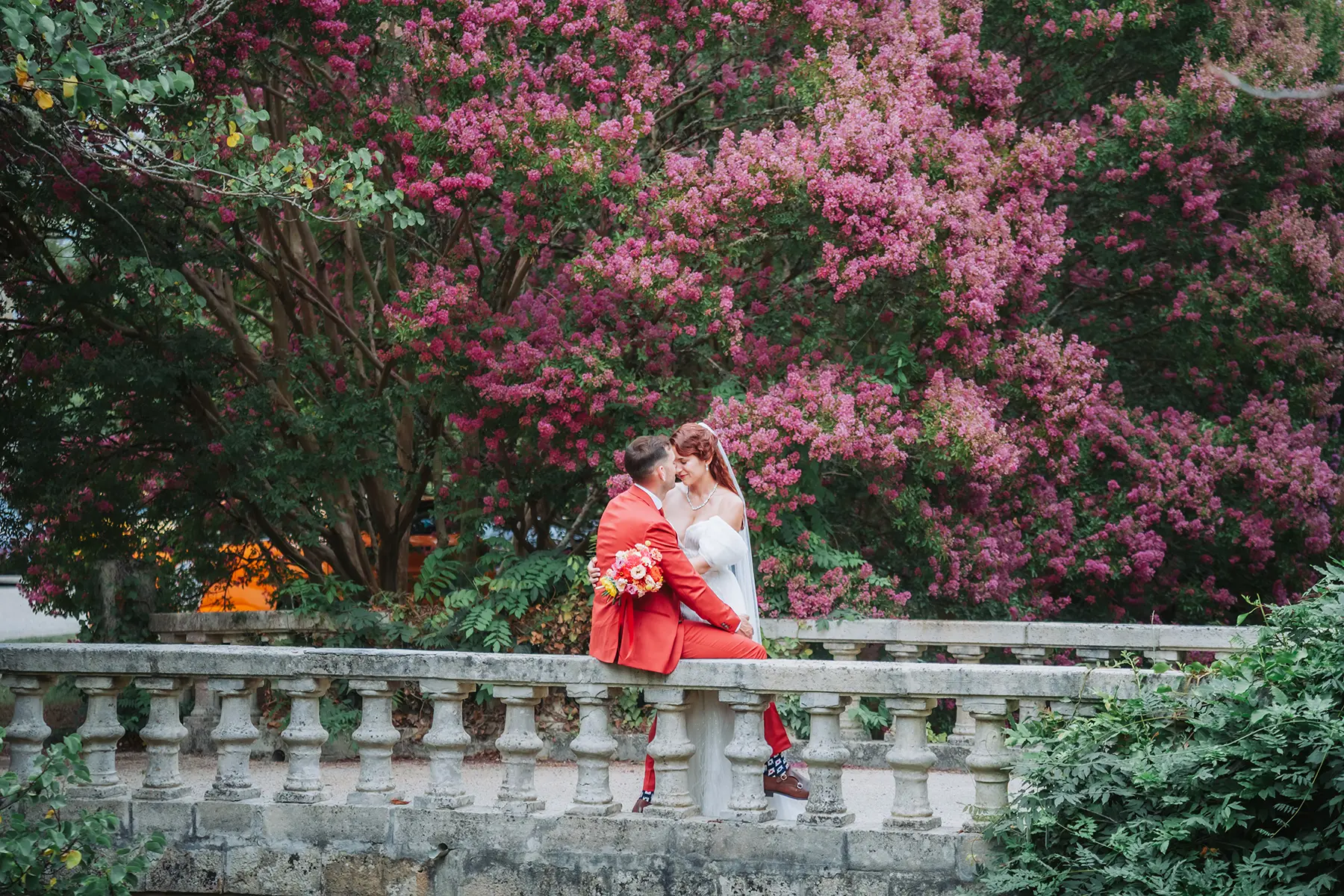 Célia & Romain 113 Mariés s'embrassant sur un pont en pierre entouré d'arbres en fleurs à Grignols