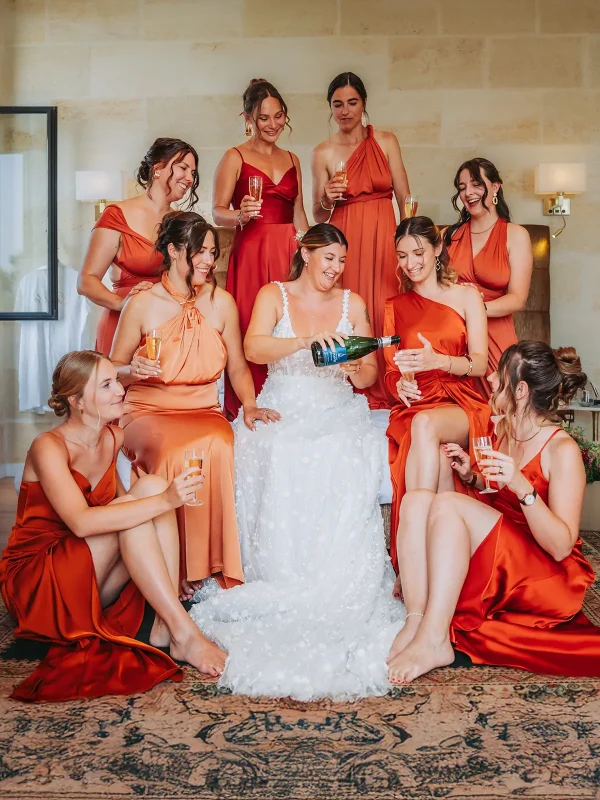 Accueil 1 La mariée entourée de ses demoiselles d'honneur en robes terracotta partageant du champagne