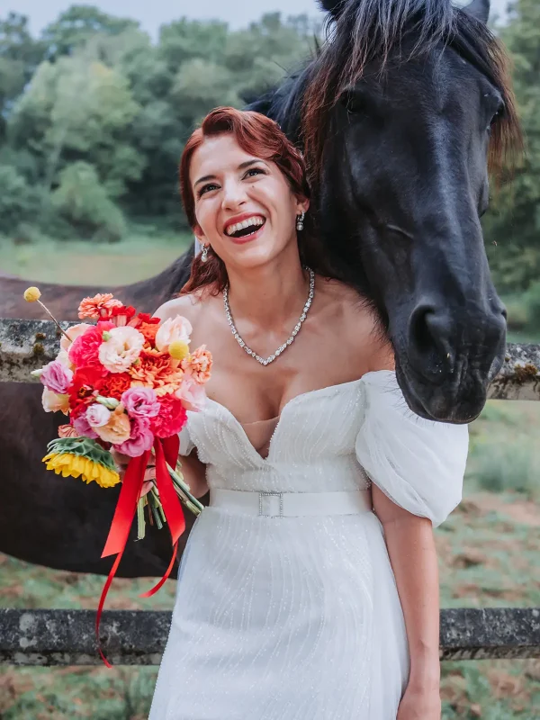 Mariée souriante posant avec un cheval noir au Domaine de la Dame Blanche à Grignols